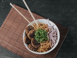 a bowl of noodles with meatballs and onions