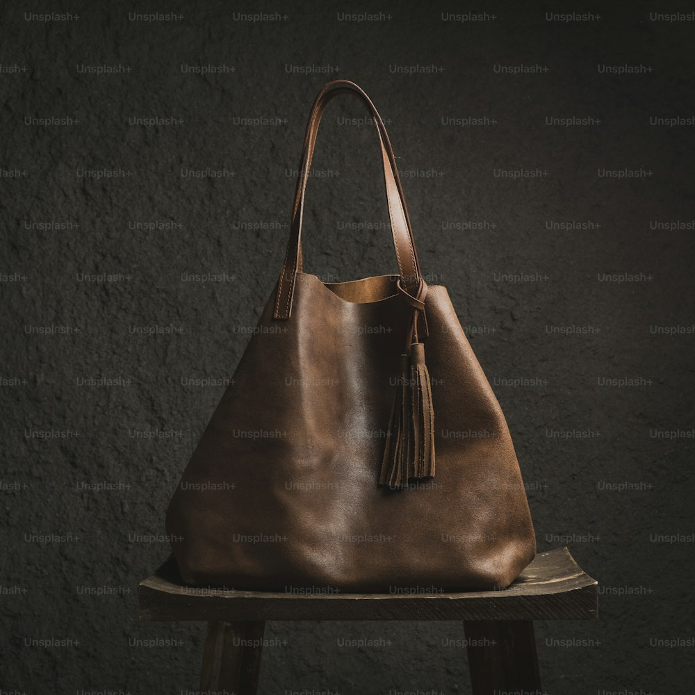 木製のスツールの上に座っている茶色の革のバッグ