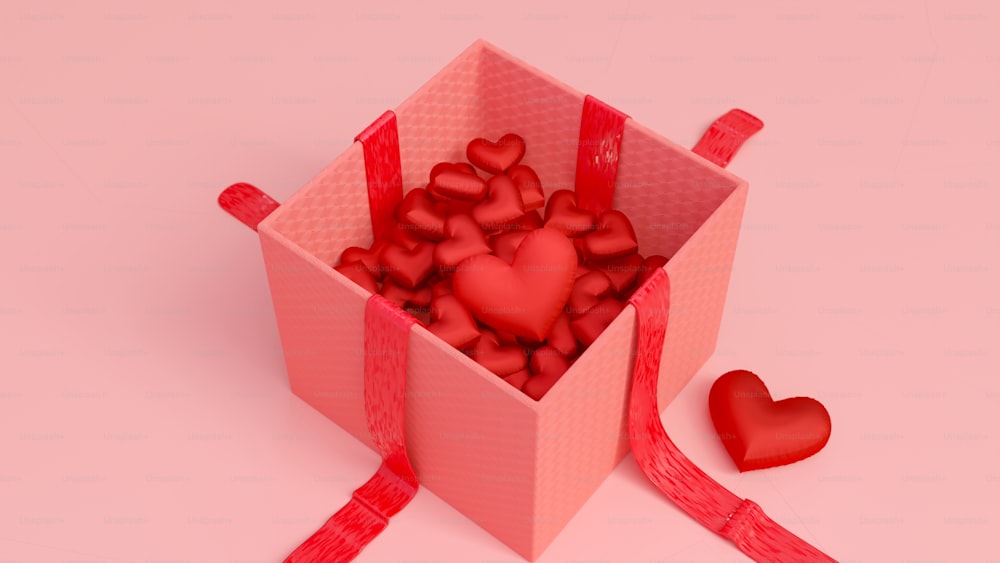 Une boîte rose remplie de cœurs rouges à côté d’un ruban rouge