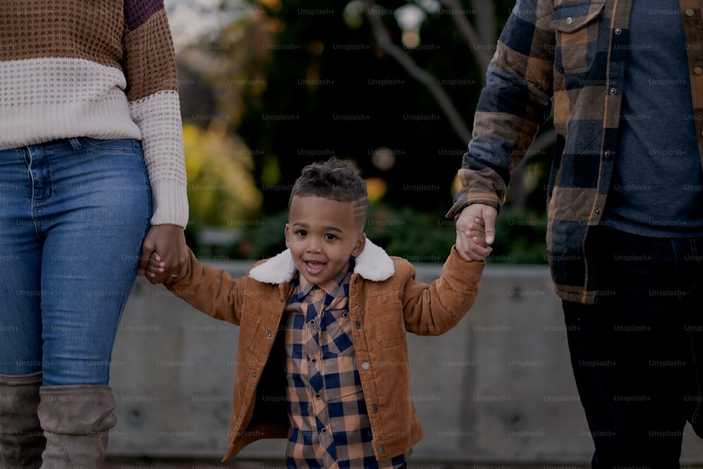 a little boy holding the hands of his parents