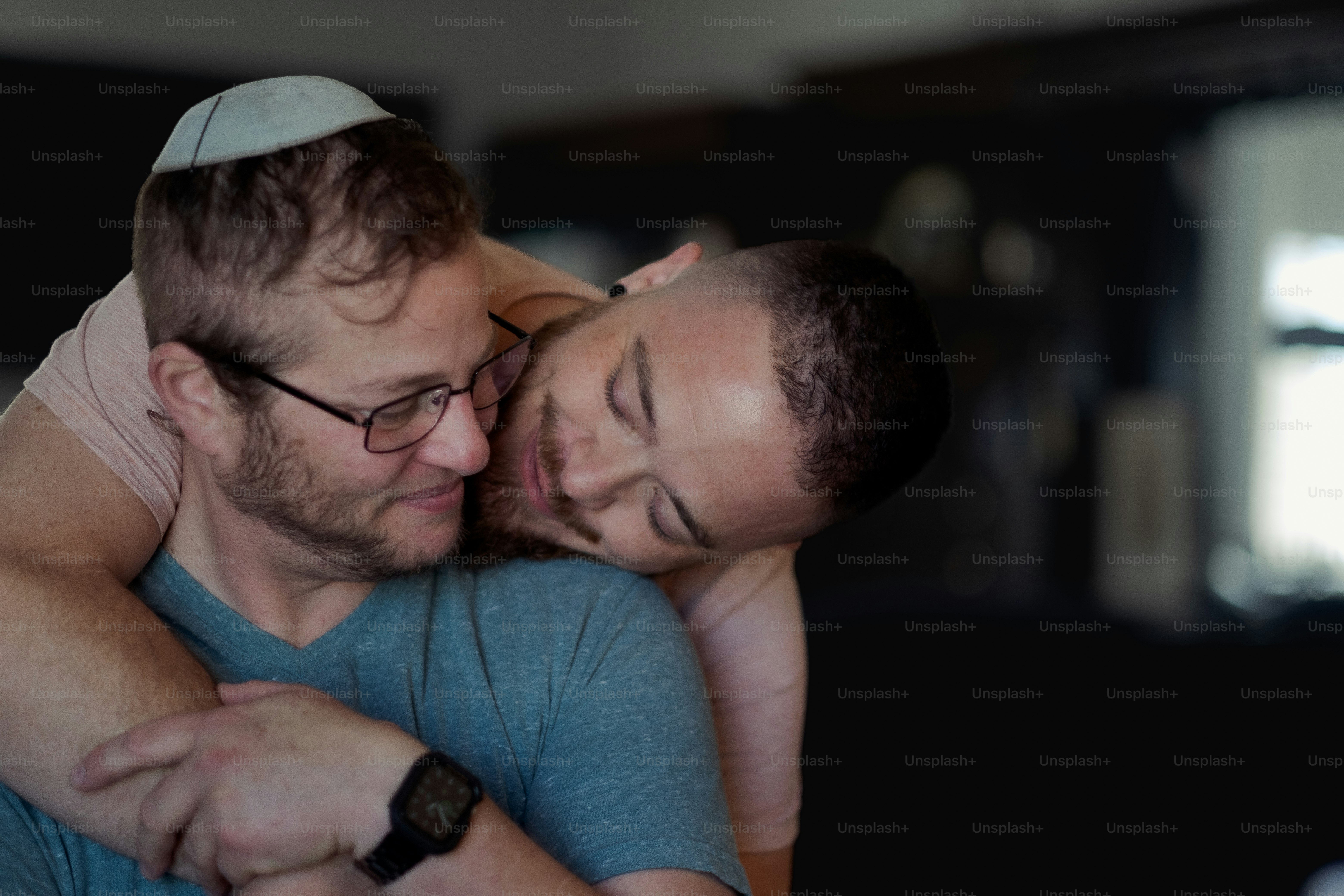 Joshua and Rafi at their home, expressing their love and affection for one other. They maintain a Jewish household for themselves and for their children. Both Joshua and Rafi are active in Jewish causes, and are men of trans experience.