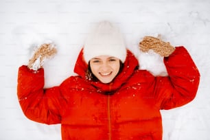 a woman in a red jacket and a white hat in the snow