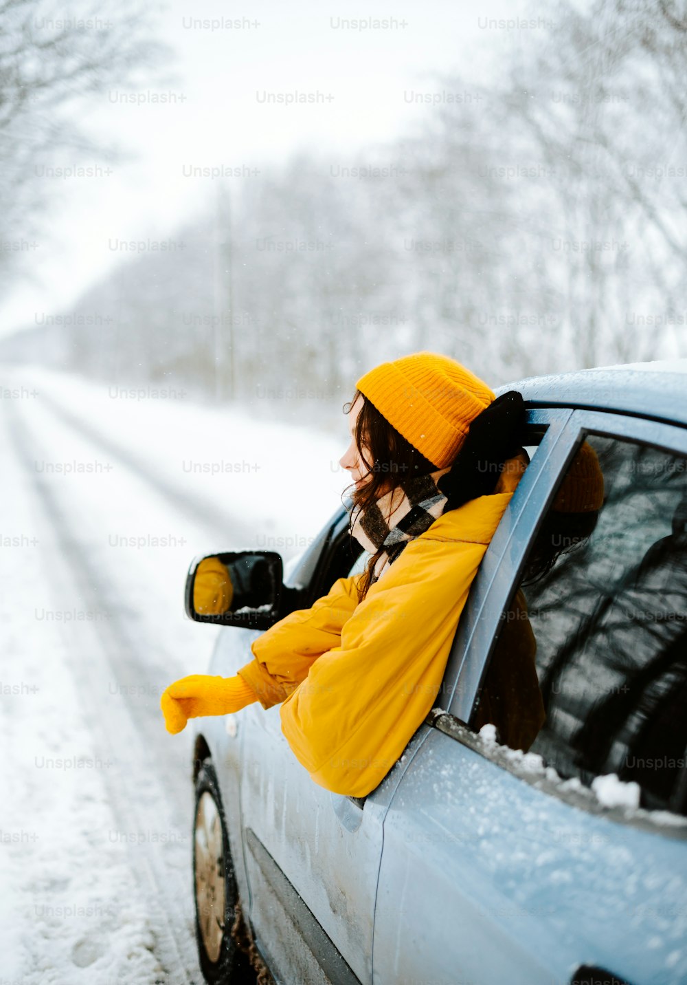 uma mulher sentada em um carro em uma estrada nevada