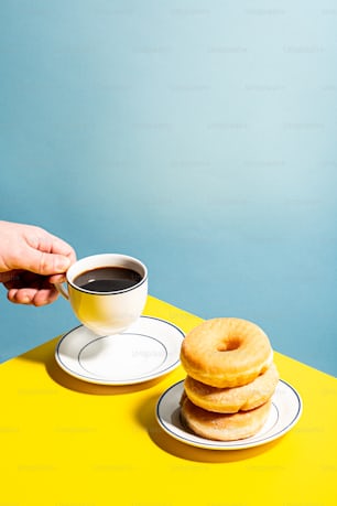 a person holding a cup of coffee next to a stack of doughnuts