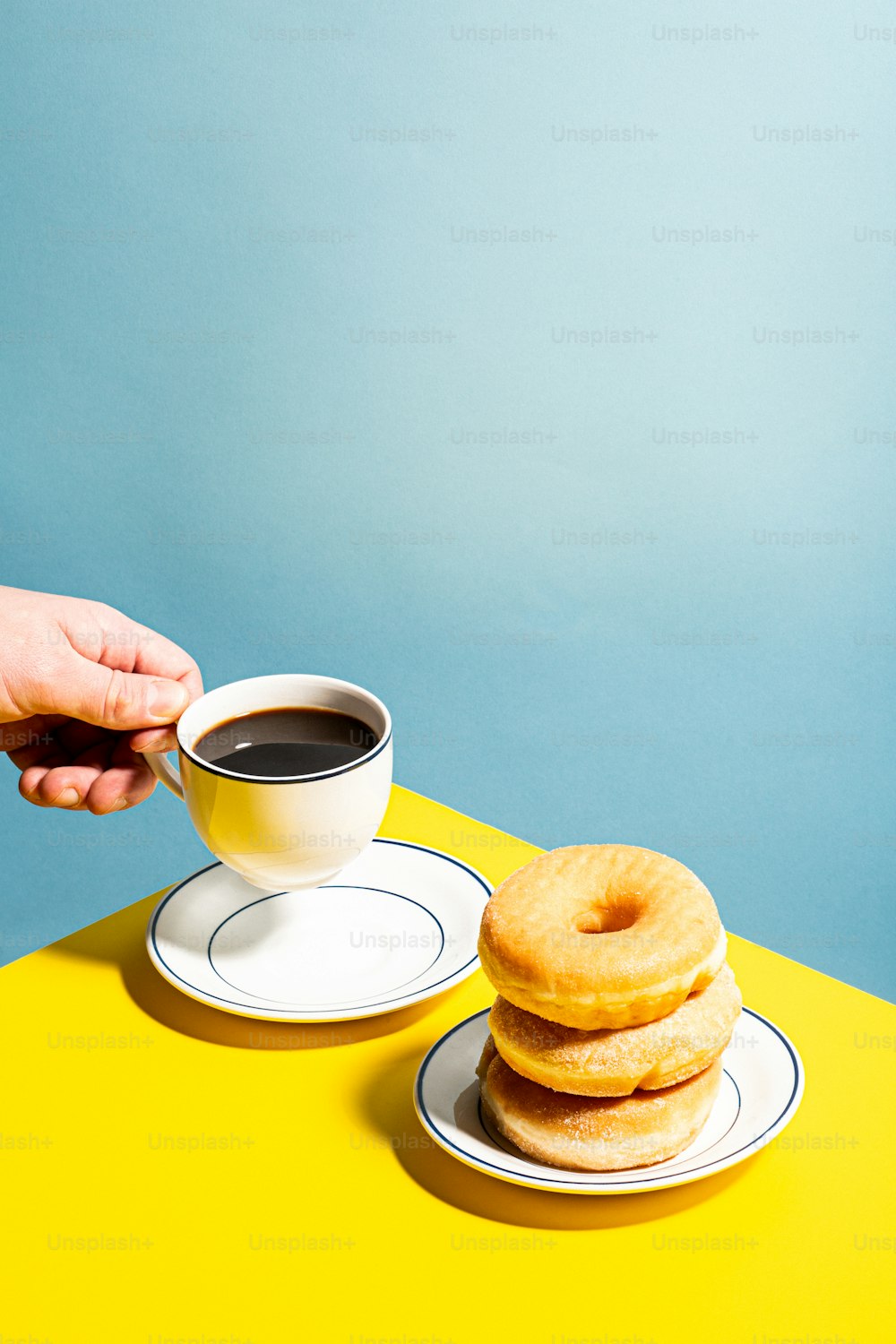 a person holding a cup of coffee next to a stack of doughnuts