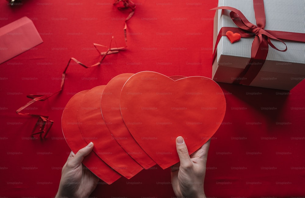 a person holding a red heart in front of a gift box