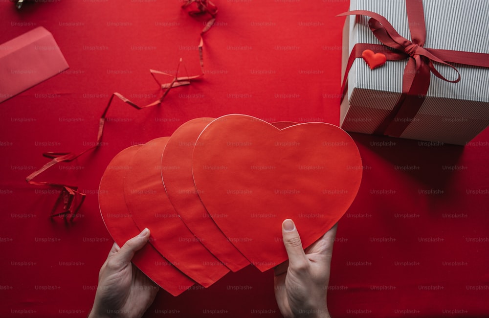 a person holding a red heart in front of a gift box