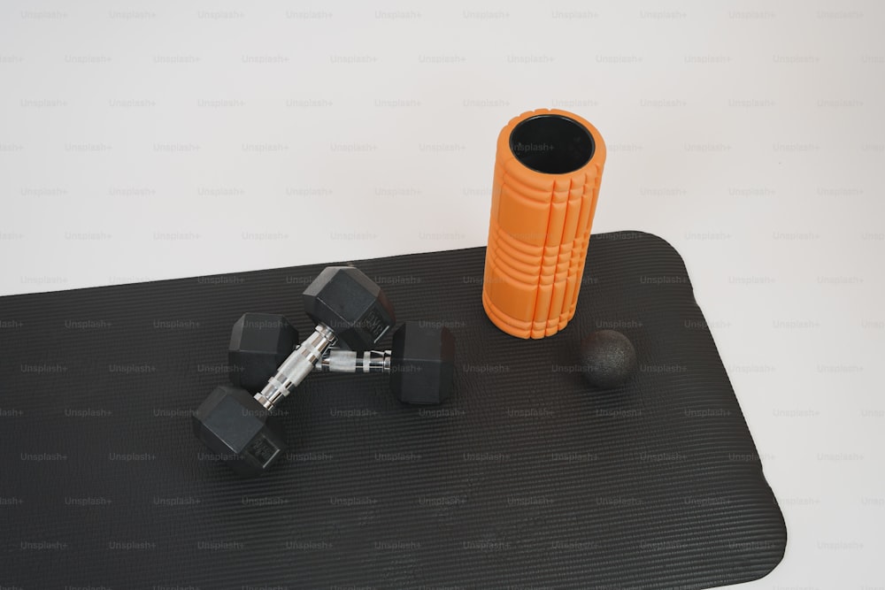 a black mat with a pair of dumbs and an orange cup