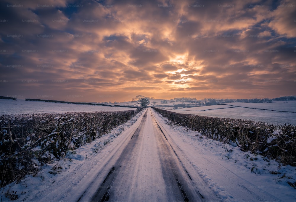 a snow covered road with a sunset in the background