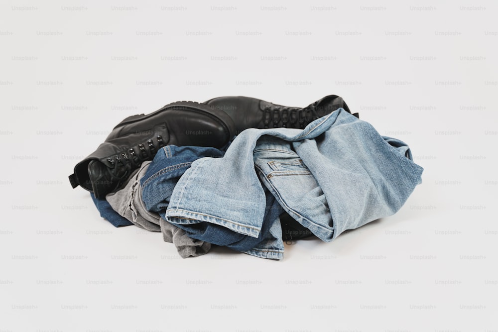 Ein Paar schwarze Lederstiefel sitzt auf einem Stapel blauer Jeans