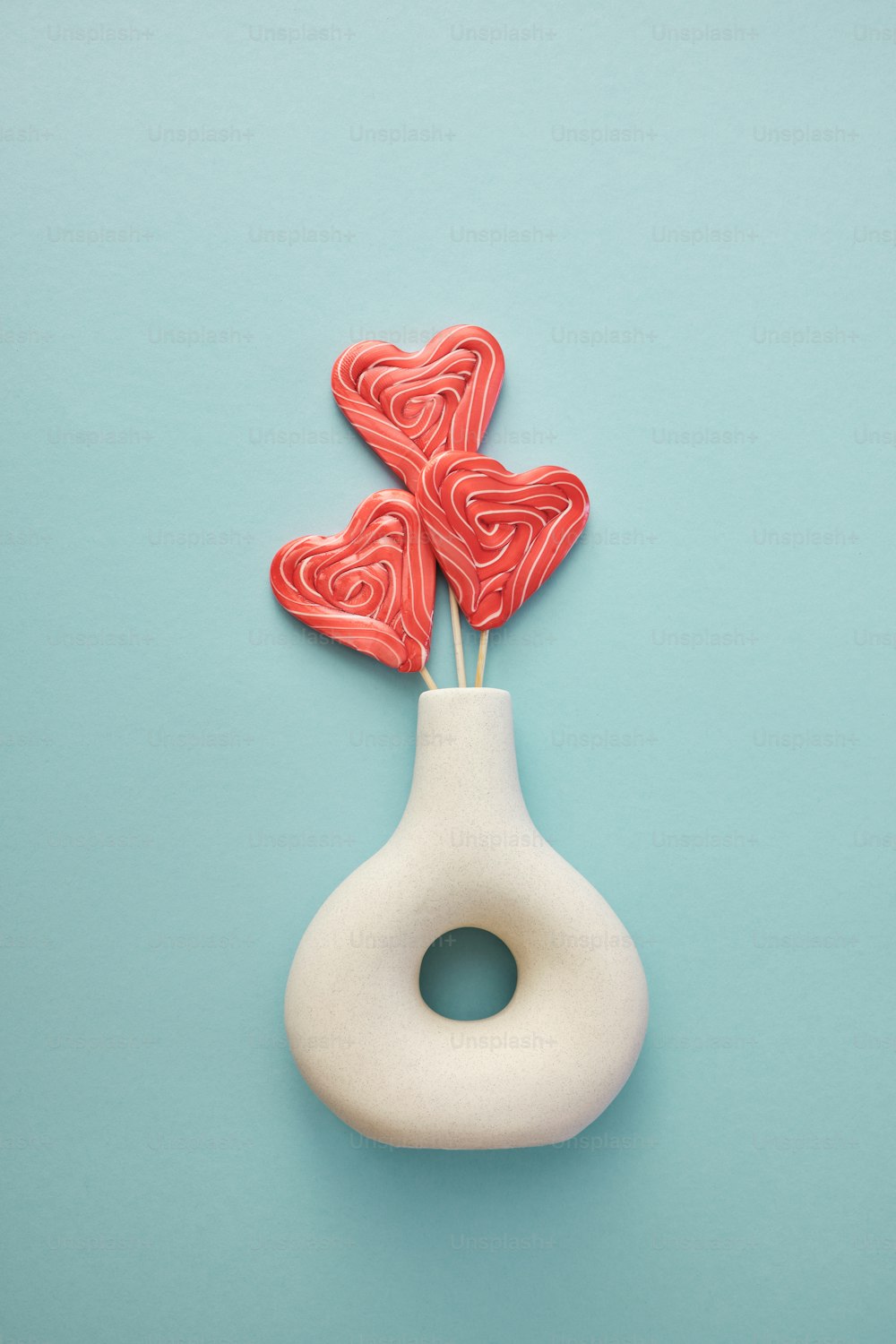 a white vase with two red heart shaped lollipops in it
