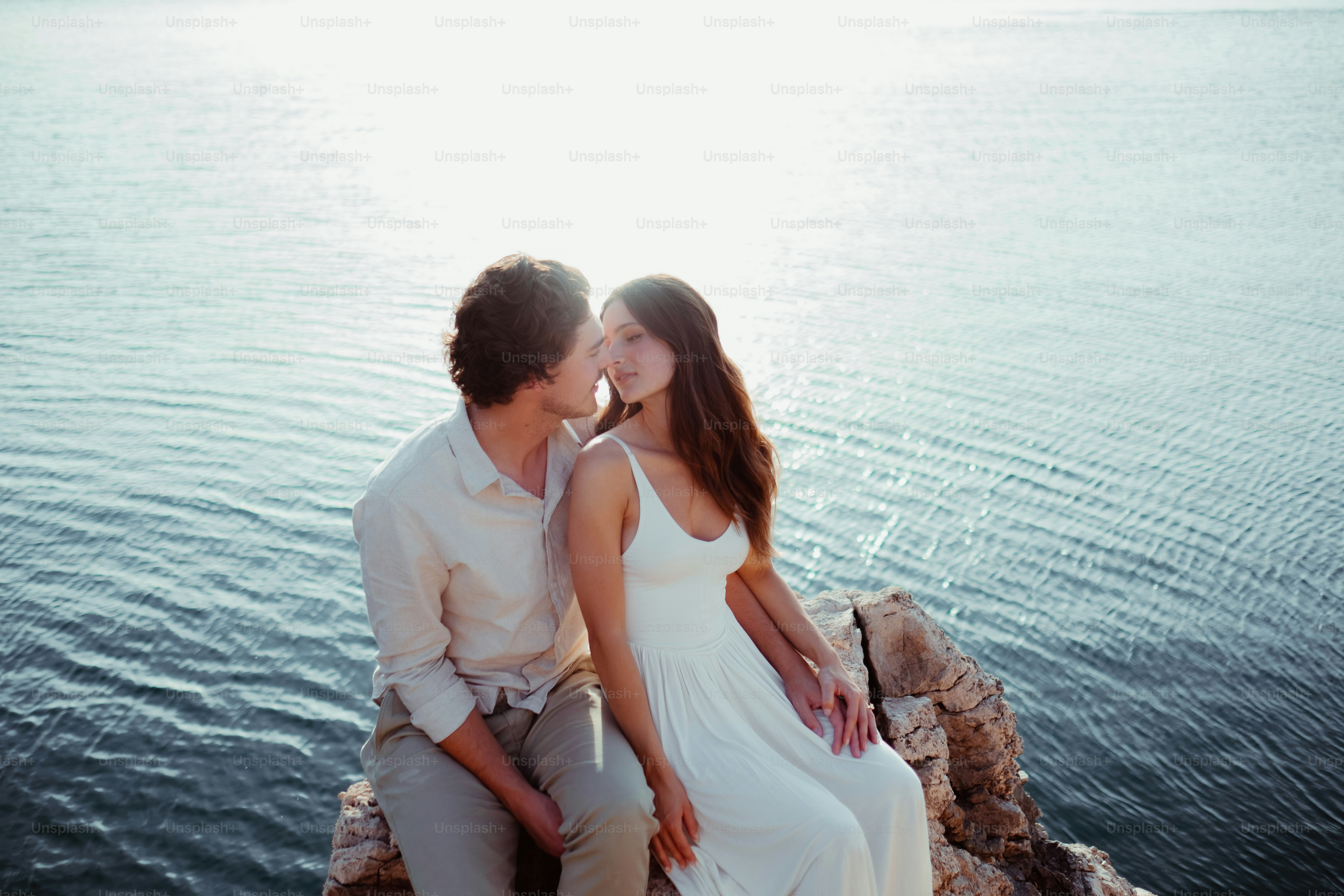 a man and a woman sitting on a rock by the water