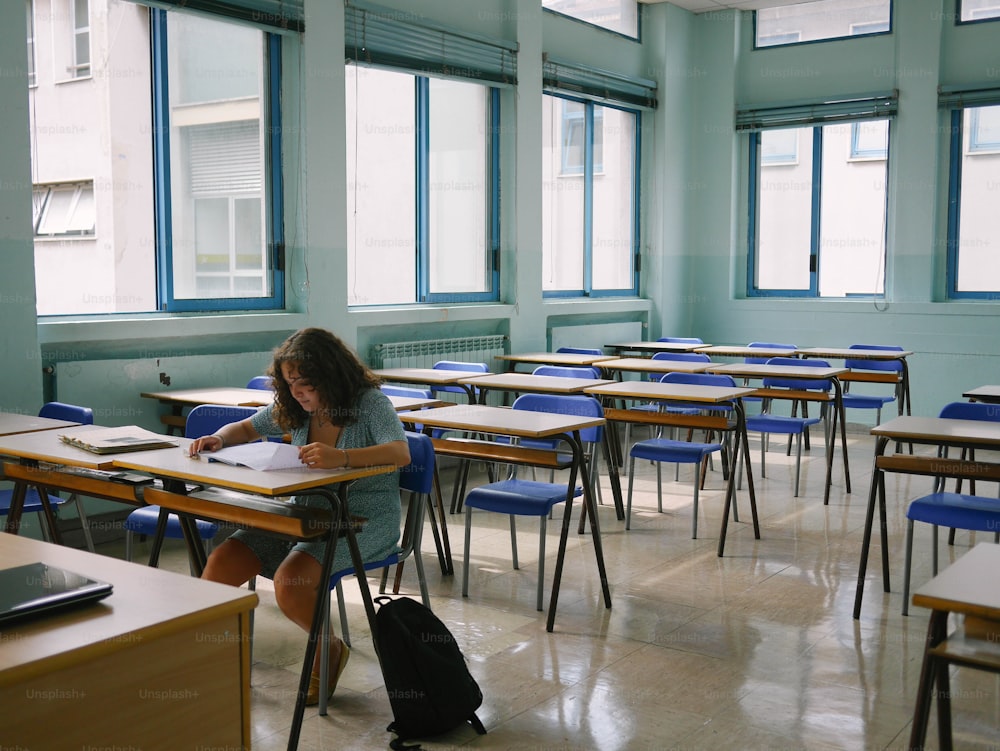 Eine Frau sitzt an einem Schreibtisch und schreibt in einem Klassenzimmer