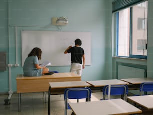 a couple of people sitting at desks in a classroom