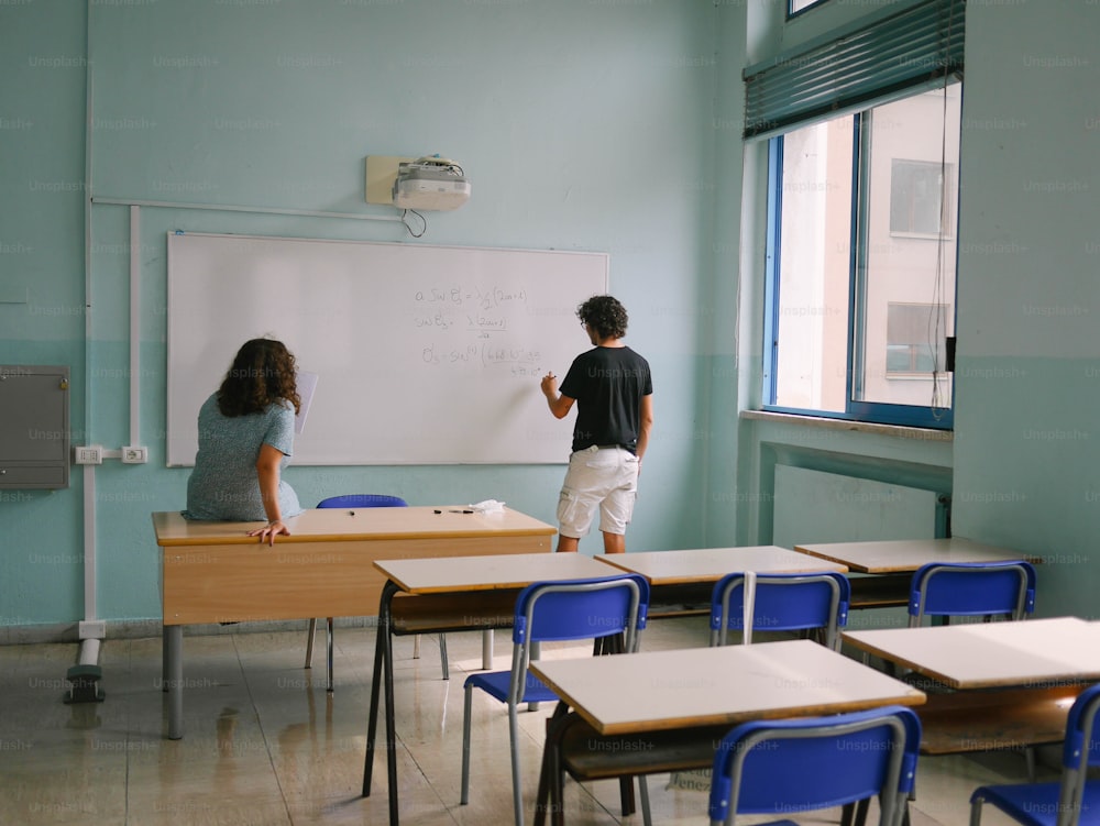 a boy and a girl standing in front of a whiteboard in a classroom