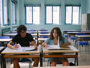 Ein Mann und eine Frau sitzen an Schreibtischen in einem Klassenzimmer