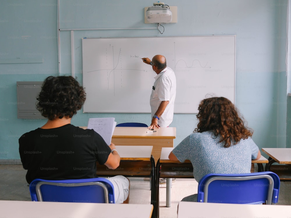 a group of people sitting at desks in front of a whiteboard