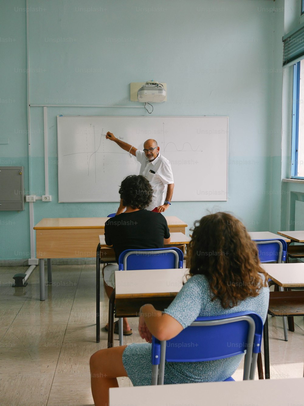 um homem em pé na frente de um quadro branco em uma sala de aula