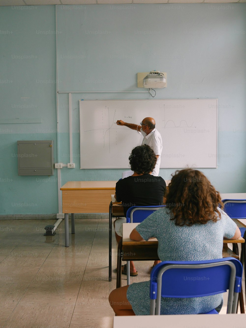 a group of people sitting at desks in front of a whiteboard