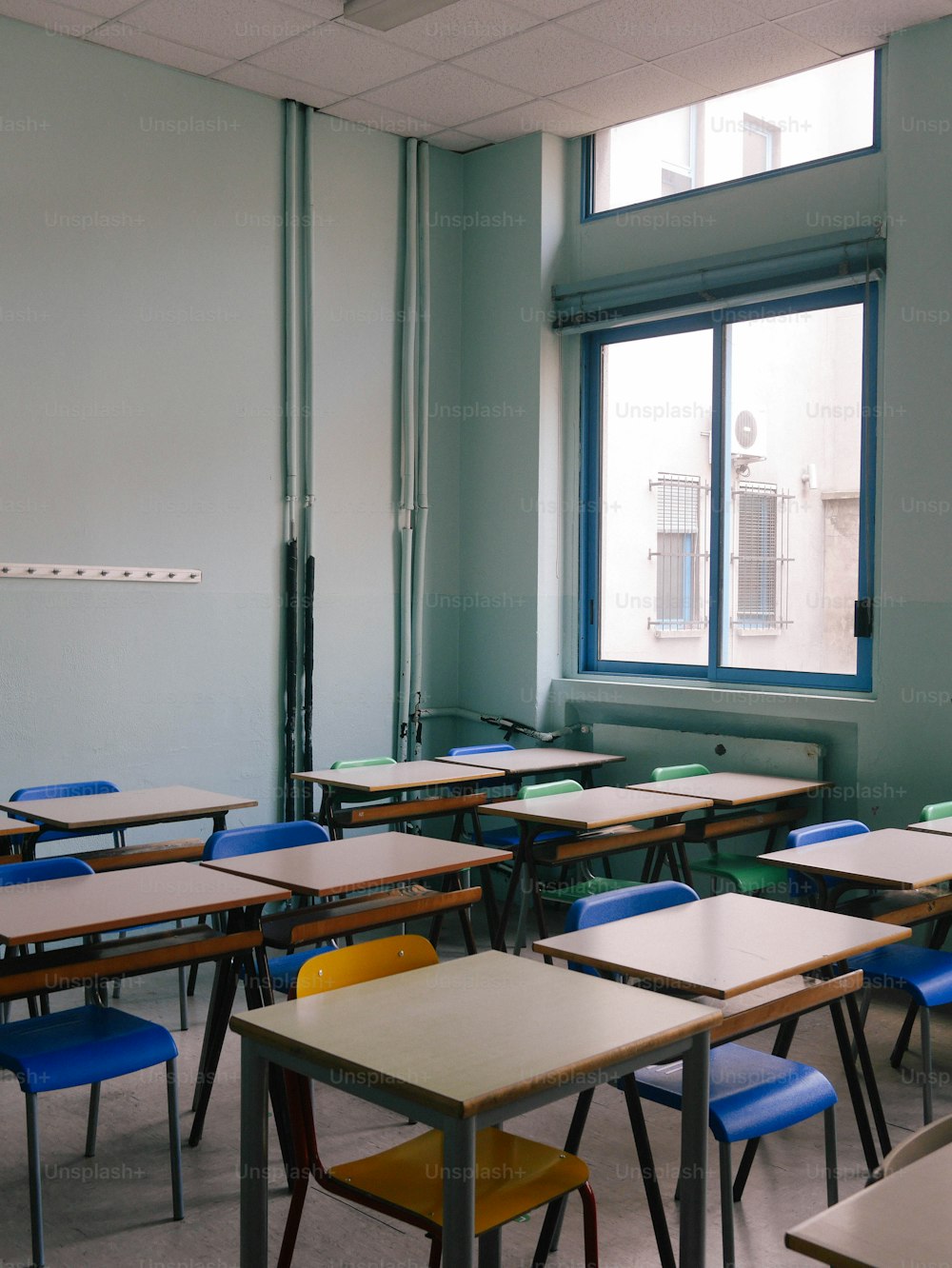 Ein Klassenzimmer voller Schreibtische und Stühle neben einem Fenster