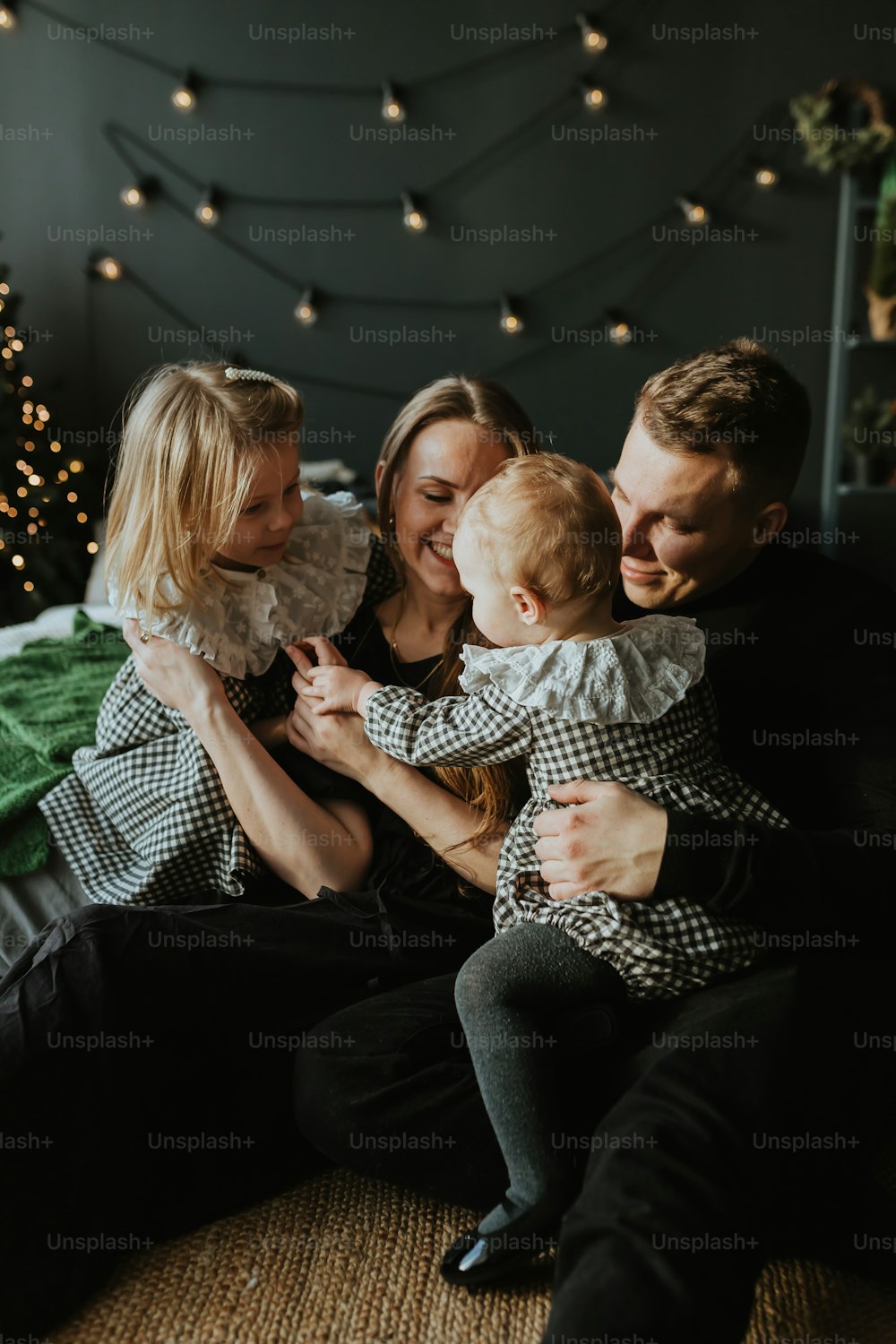 uma família sentada em uma cama com uma árvore de Natal ao fundo