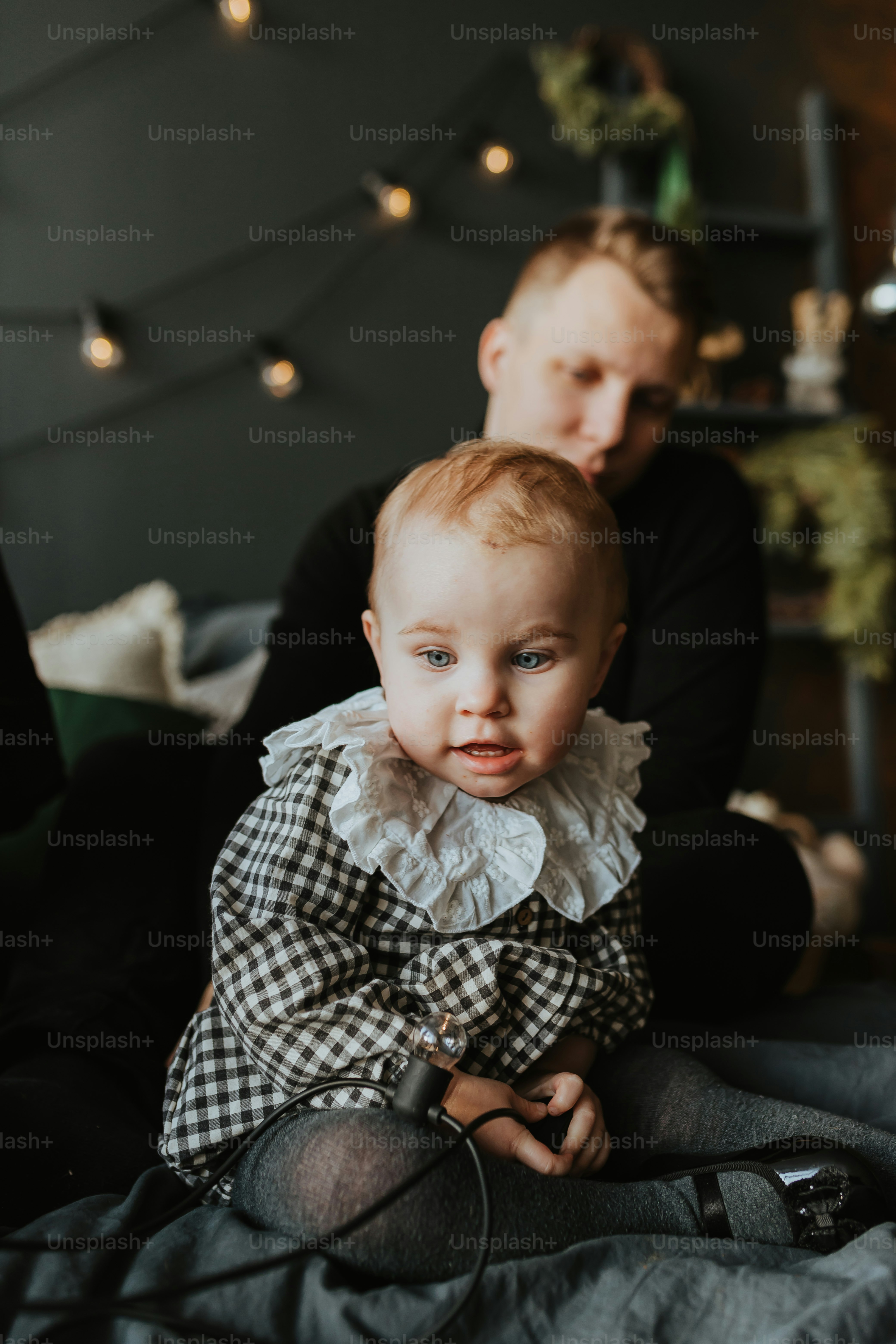 a baby sitting on a bed with a man in the background