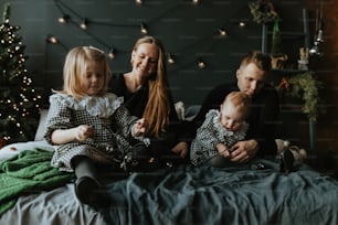 uma família de três pessoas sentada em uma cama em frente a uma árvore de Natal