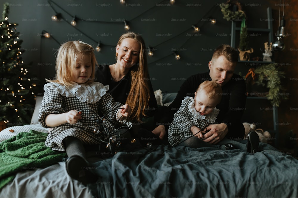 Une famille de trois personnes assise sur un lit devant un sapin de Noël