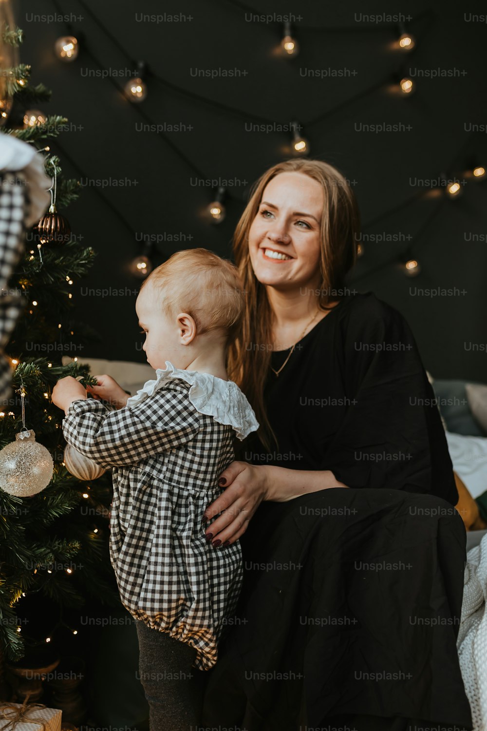 uma mulher que segura um bebê ao lado de uma árvore de Natal