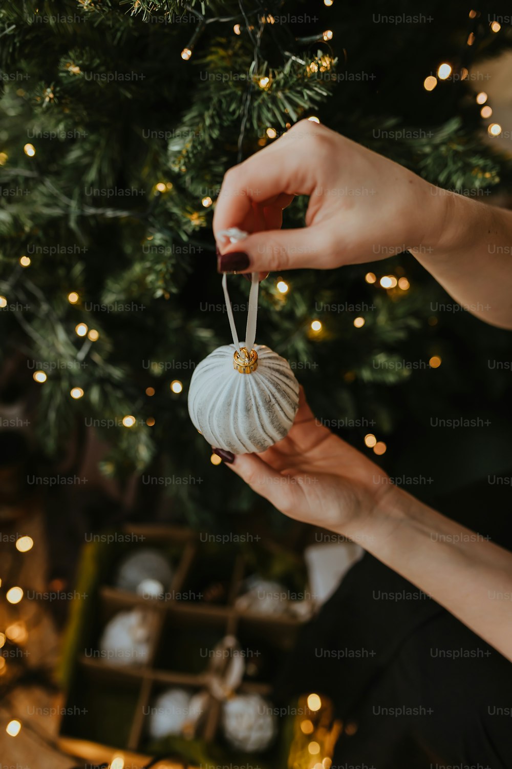 Una persona sosteniendo un adorno blanco frente a un árbol de Navidad