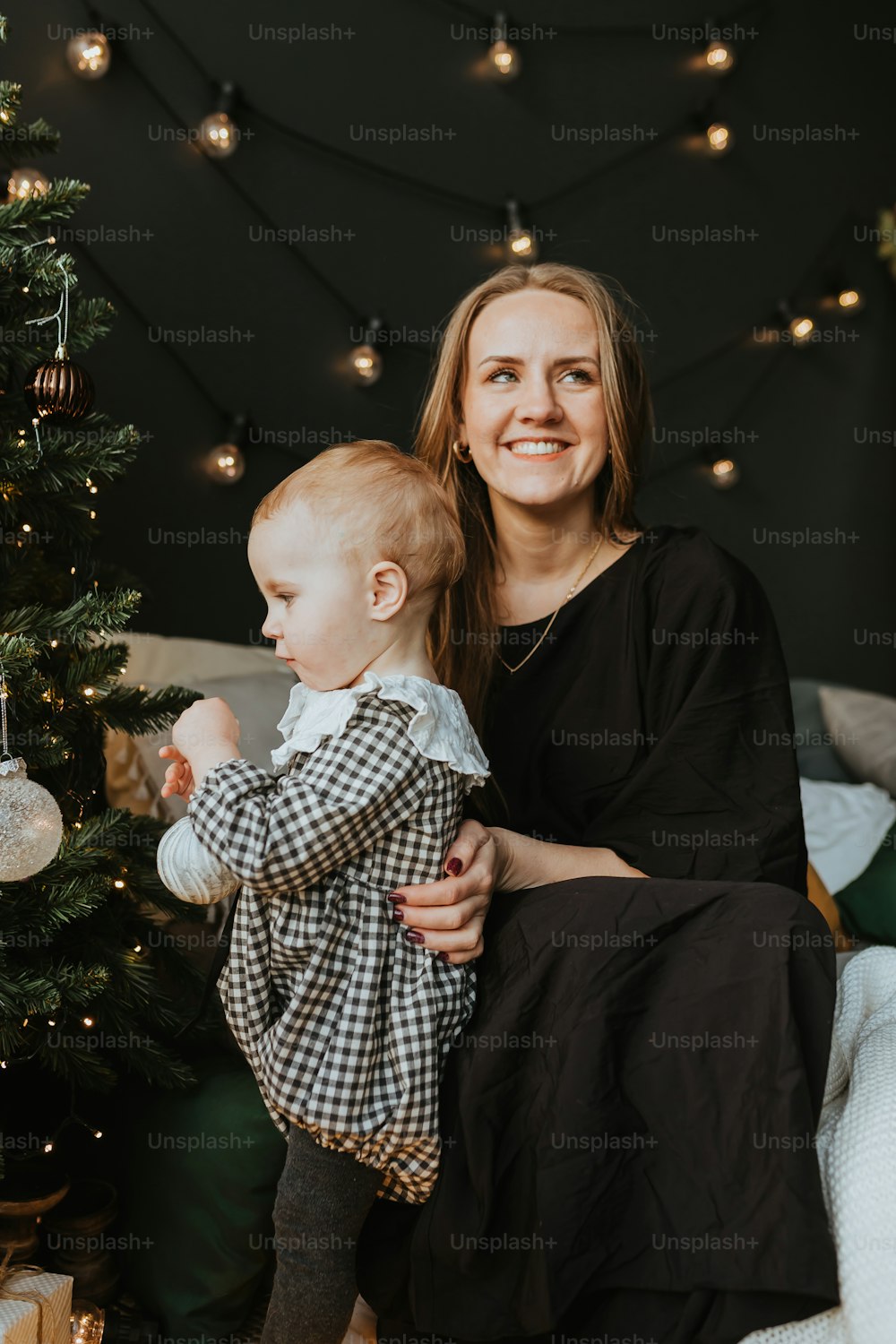 uma mulher que segura um bebê ao lado de uma árvore de Natal