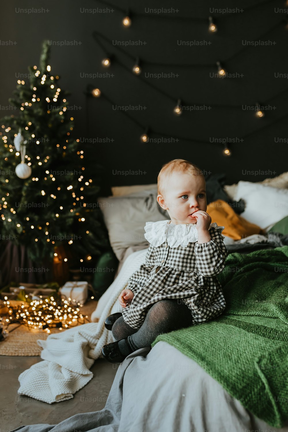 a baby sitting on a bed in front of a christmas tree