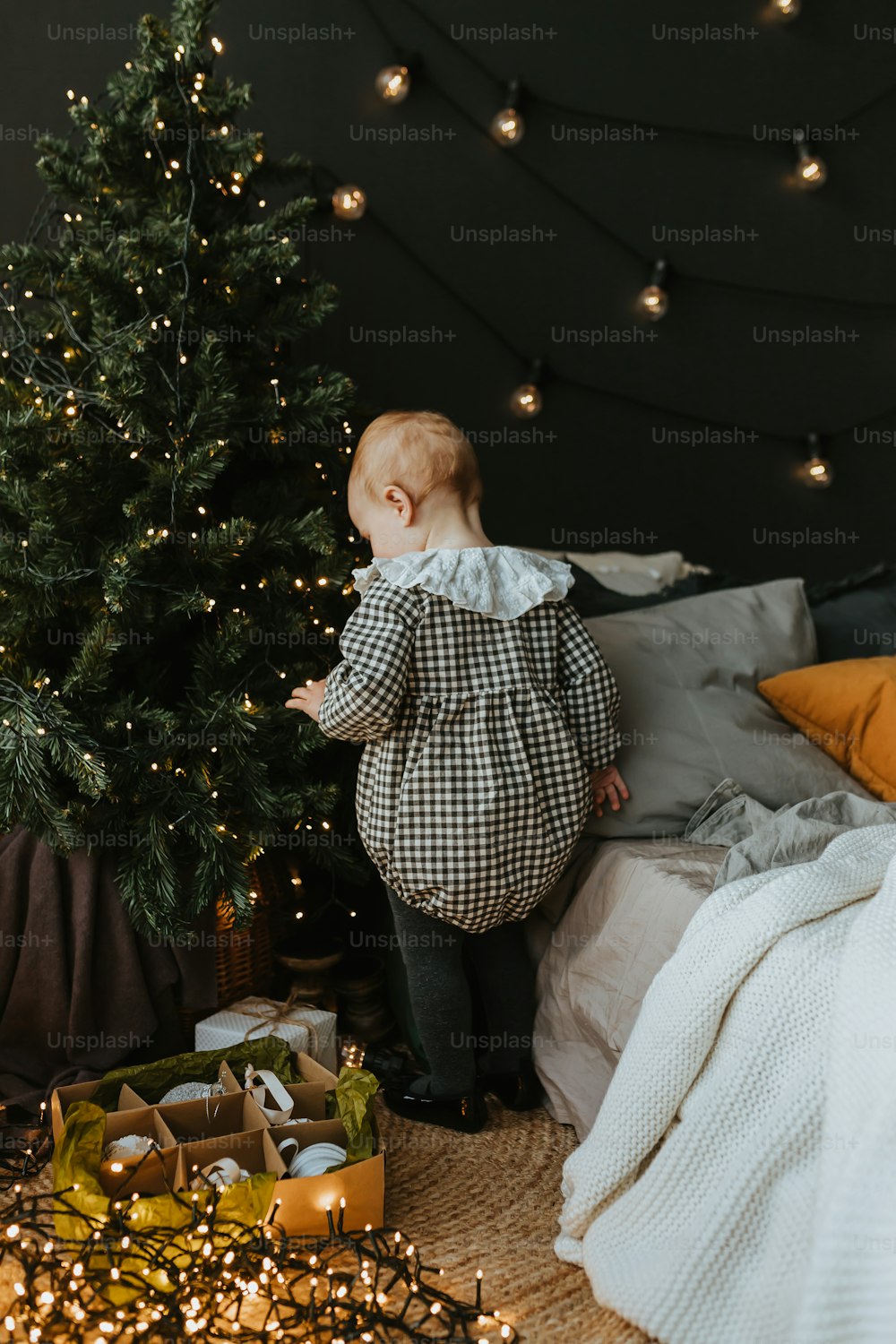 um bebê em pé ao lado de uma árvore de Natal