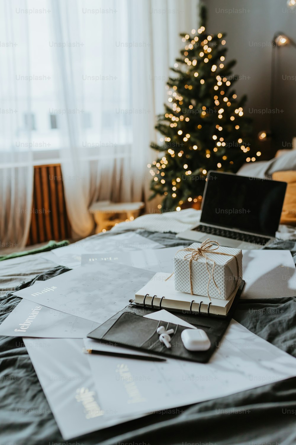 um computador portátil sentado em cima de uma cama ao lado de uma árvore de Natal