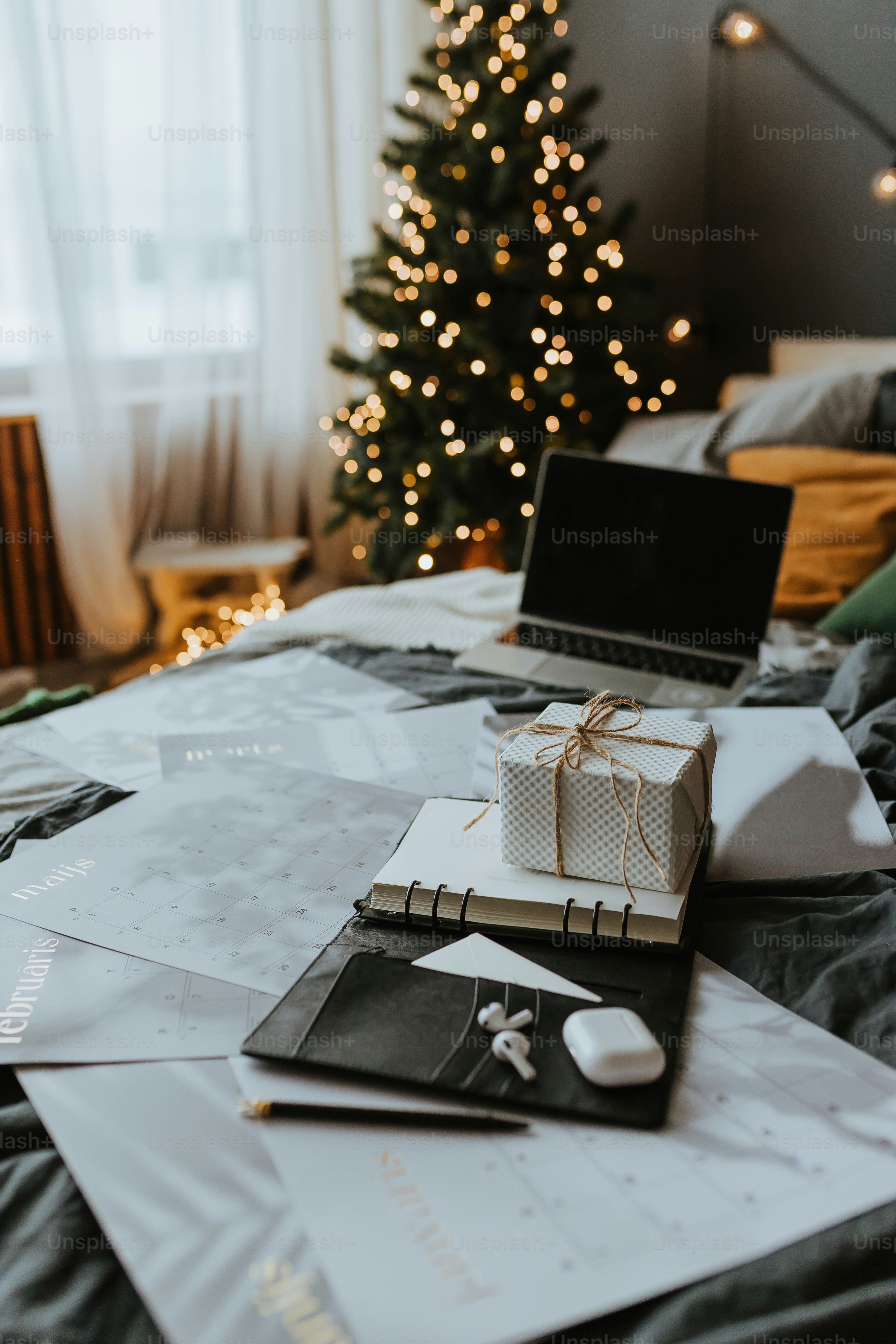 um computador portátil sentado em cima de uma cama ao lado de uma árvore de Natal