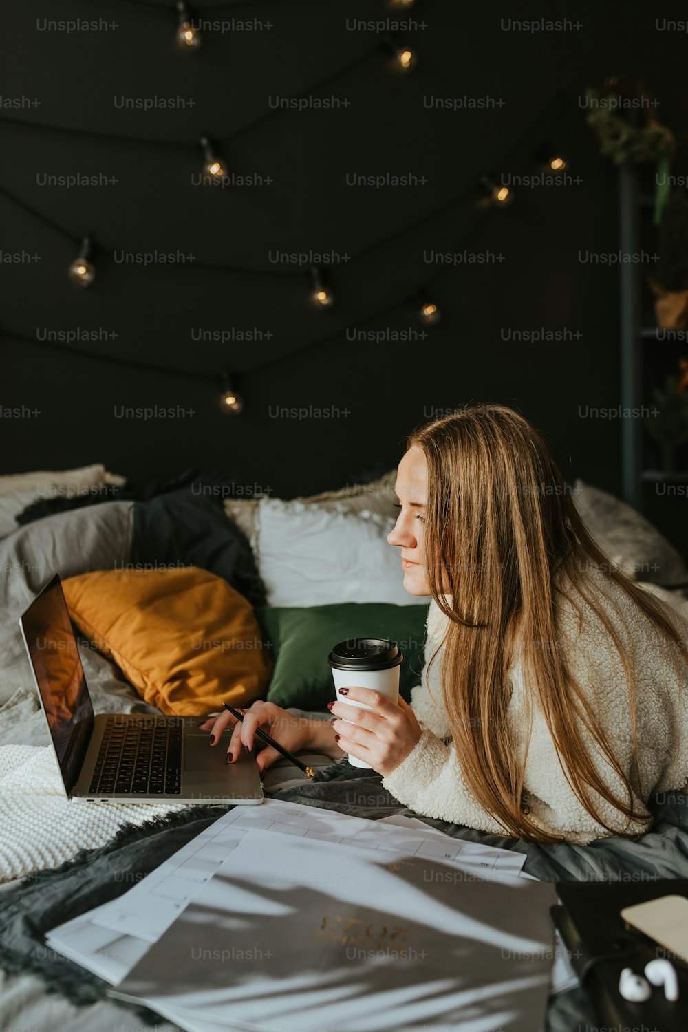 uma mulher sentada em uma cama com um laptop e uma xícara de café