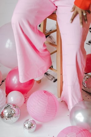 a woman in a pink dress sitting on a chair surrounded by balloons