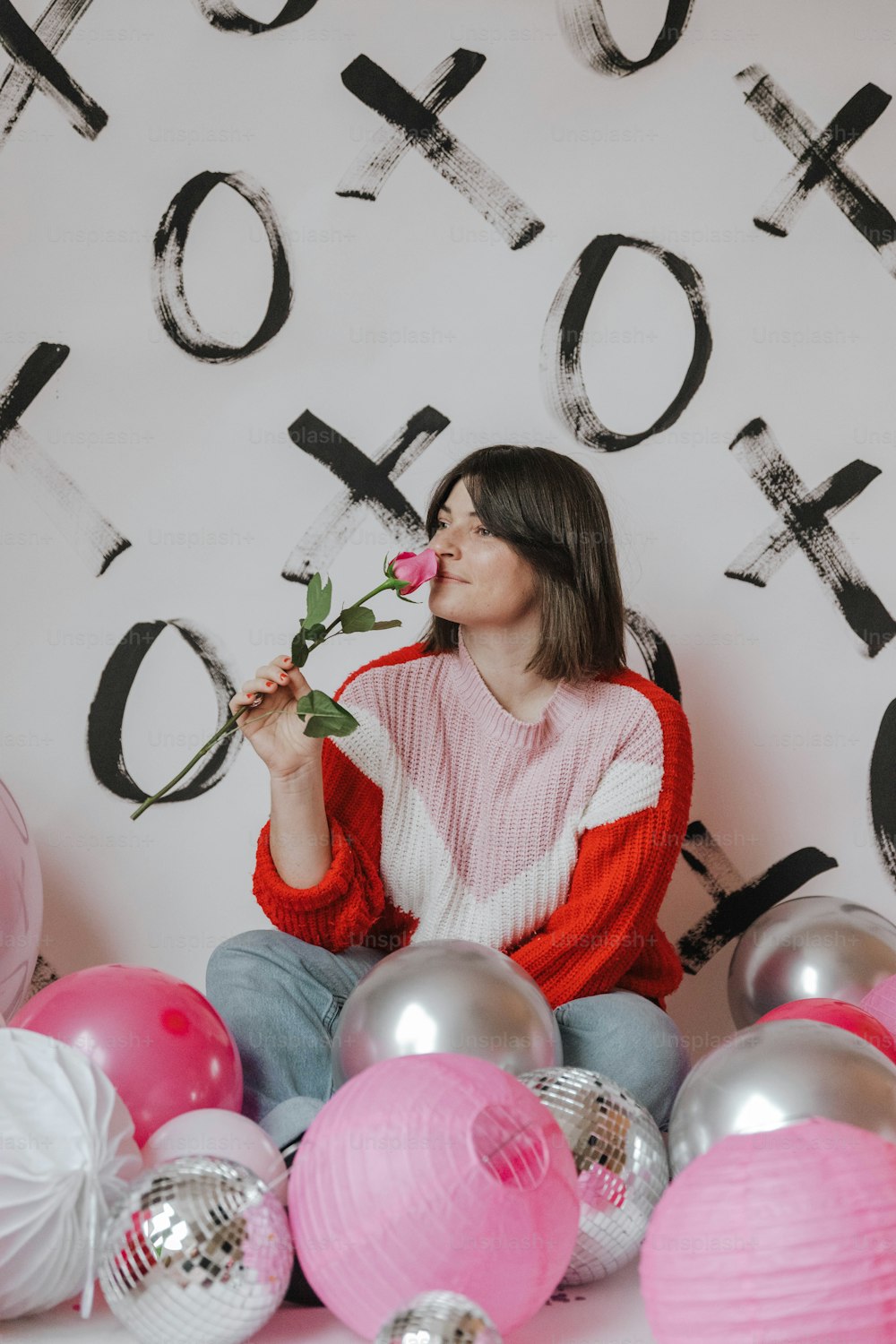 a woman sitting in front of a wall holding a rose