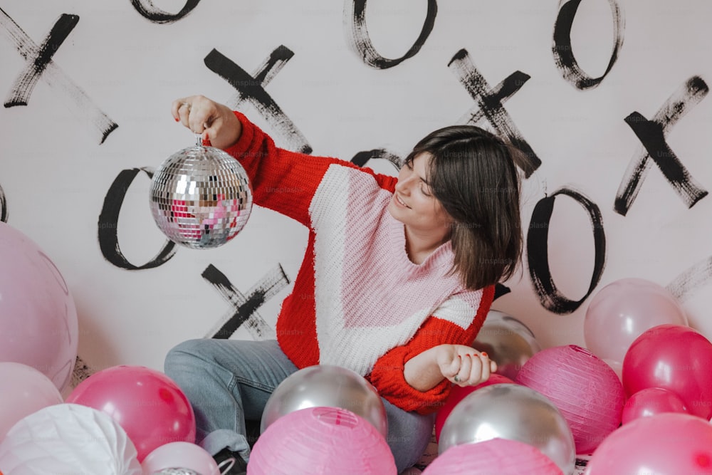 a woman holding a disco ball in front of a wall of balloons