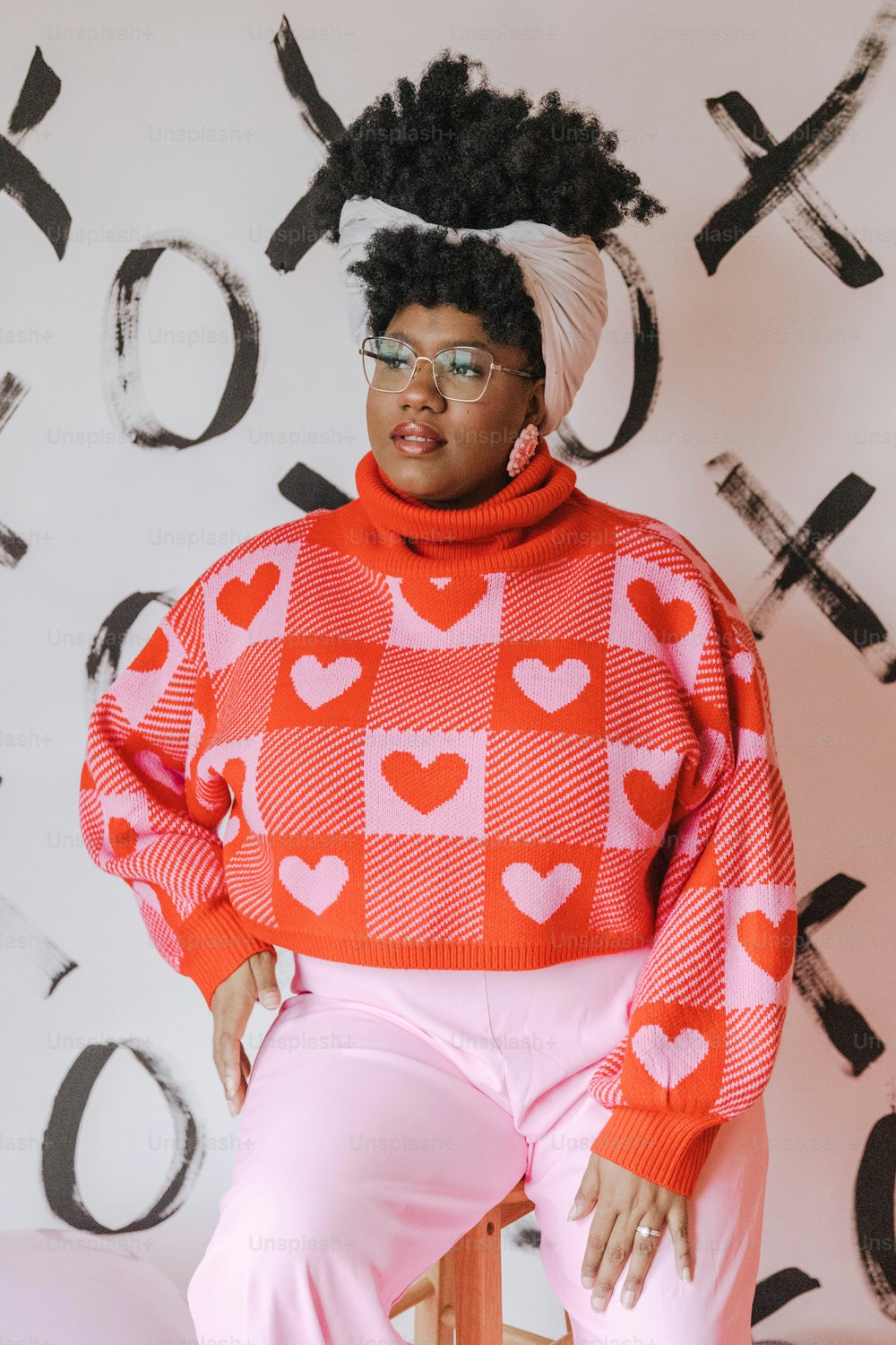 a woman sitting on a chair wearing a red and white sweater with hearts on it