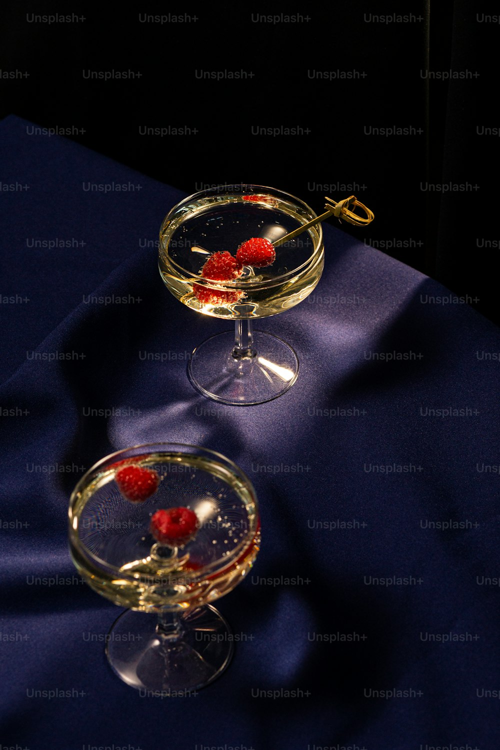 two wine glasses with rasberries in them on a blue cloth