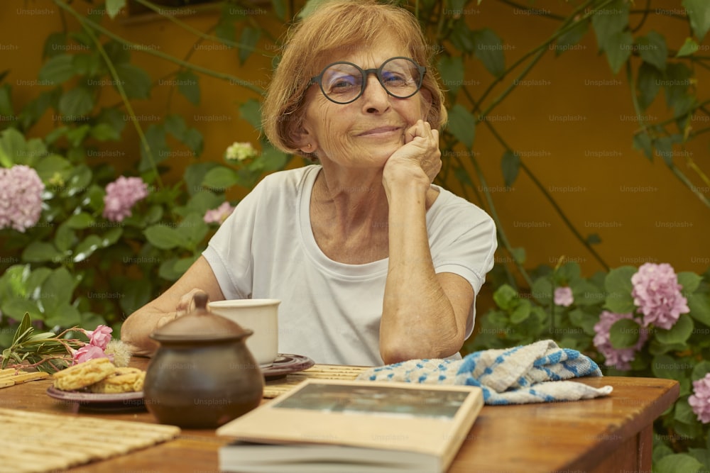 Eine Frau sitzt mit einem Buch und einer Teekanne an einem Tisch