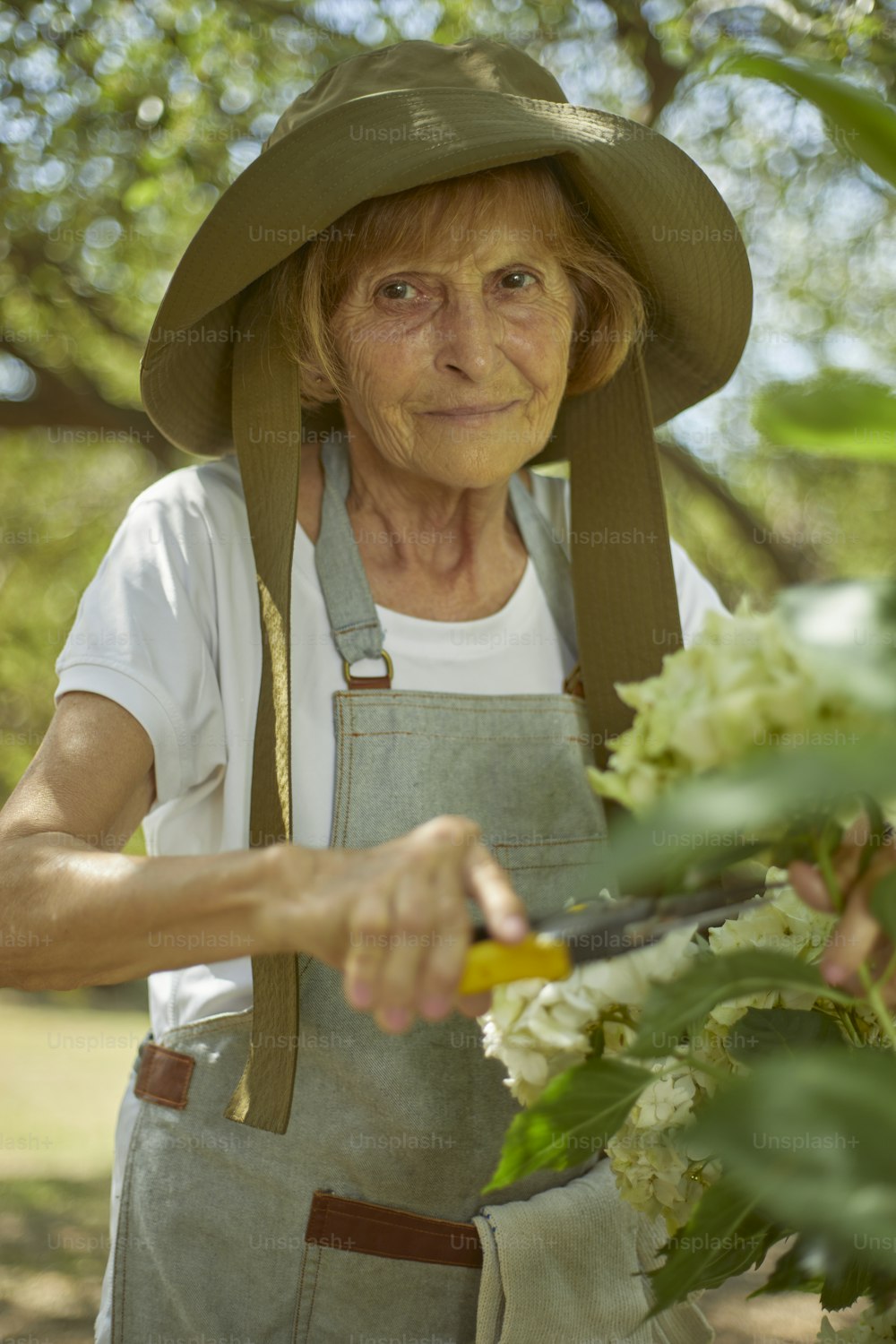 uma mulher em um chapéu cortando flores com um par de tesouras