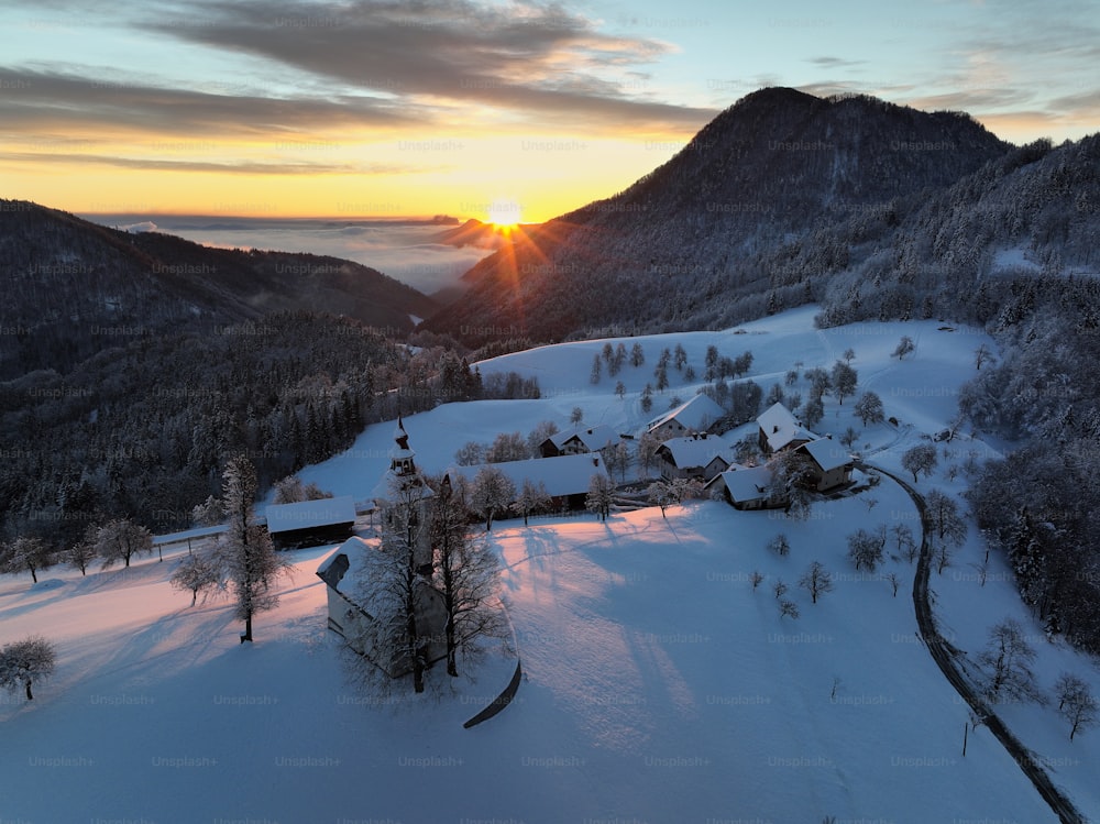 o sol está se pondo sobre uma aldeia montanhosa nevada