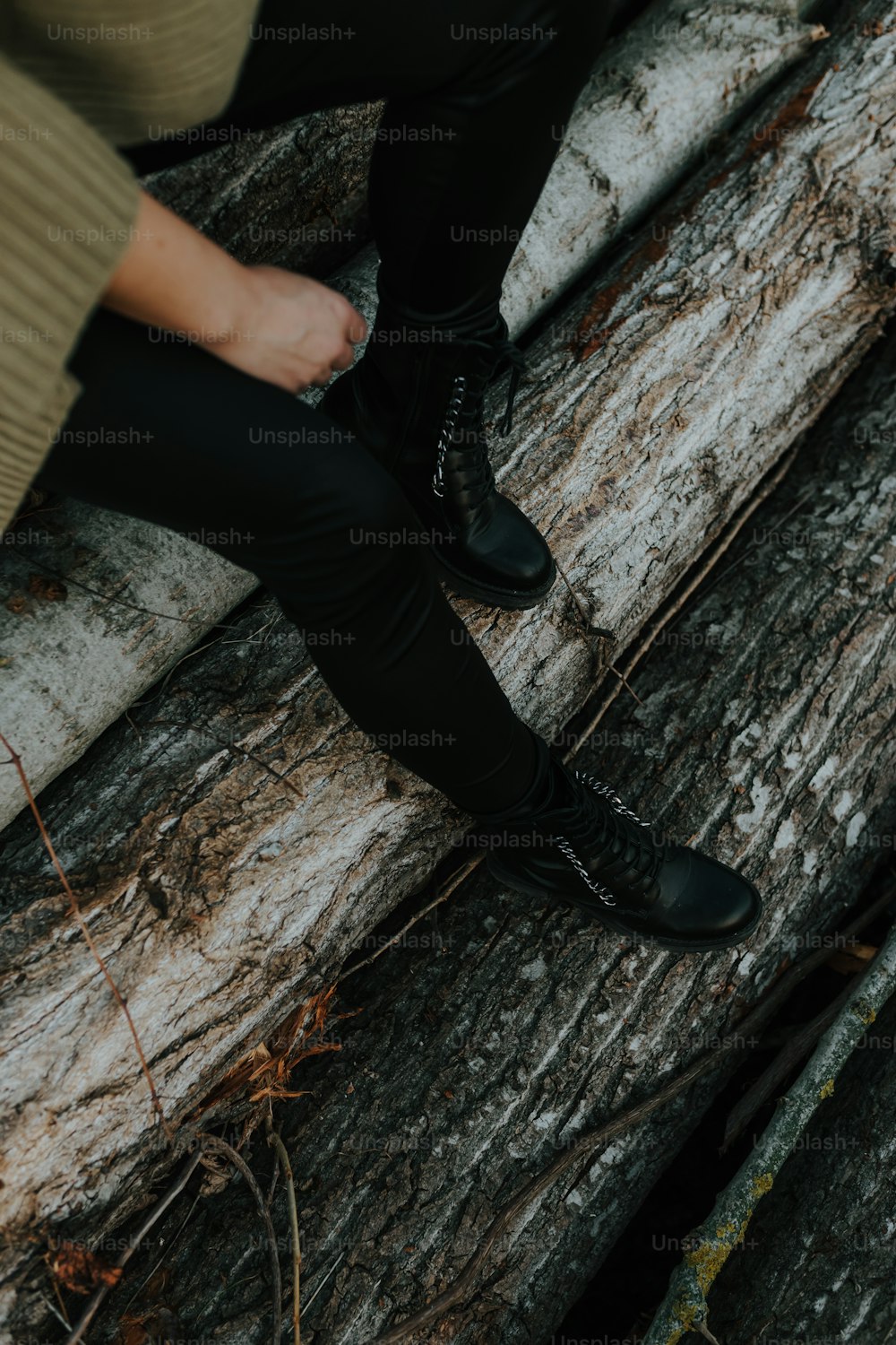 a person sitting on a tree trunk wearing black boots