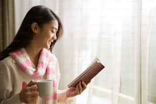 朝、本を読み、コーヒーを飲むアジア人女性。