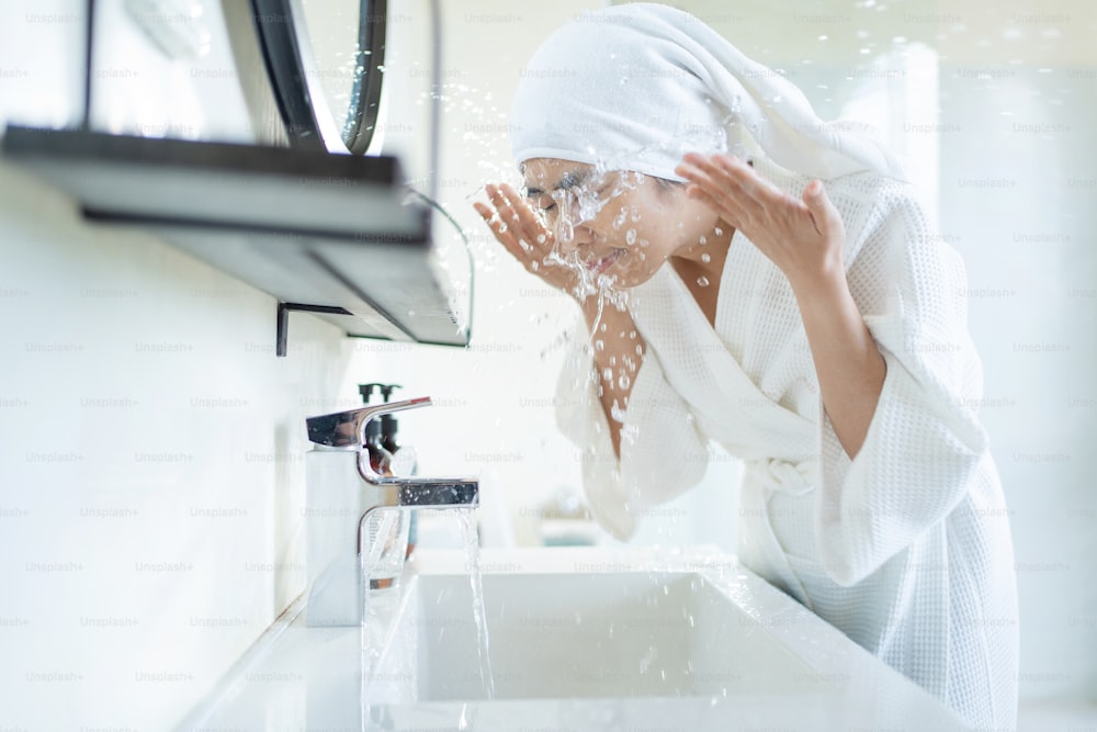 Mujer asiática lavándose la cara en el baño