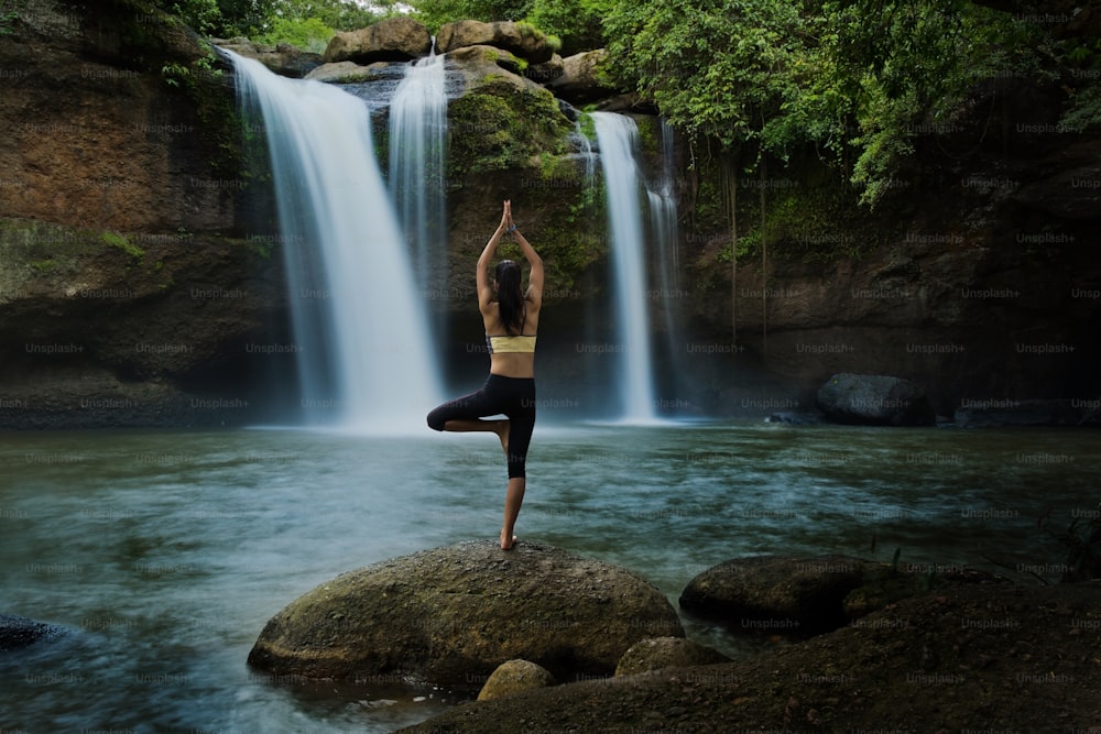 Giovane donna in una posa yoga alla cascata, si sentiva rilassata. L'esercizio