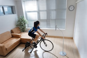 運動するアジア人女性は、屋内で自転車に乗る。悪天候時