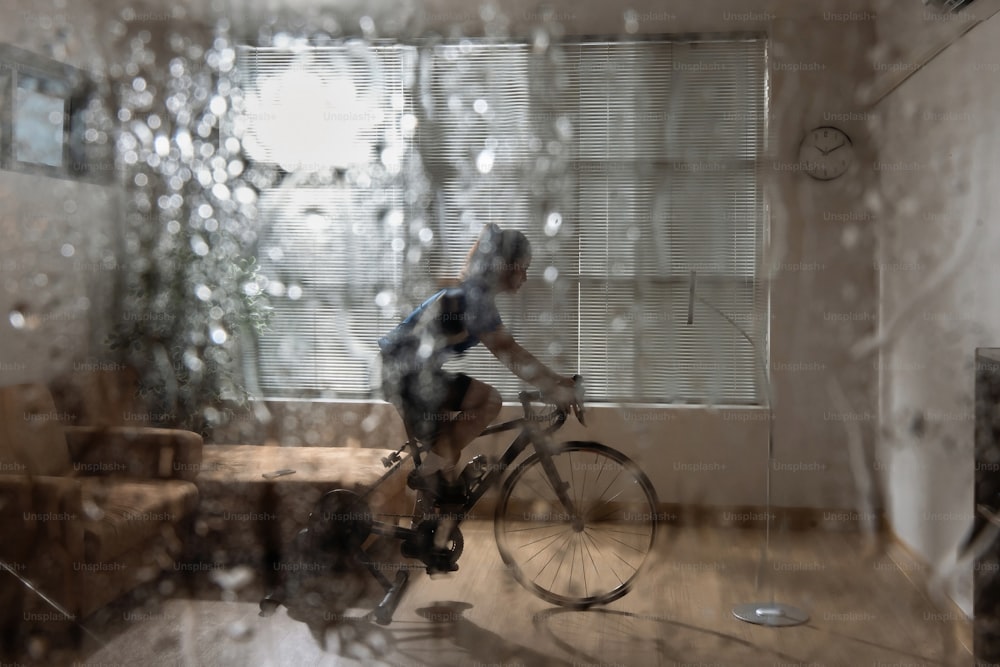 아시아 여자 사이클리스트. 그녀는 집에서 운동하고 있습니다. 트레이너에서 자전거를 타고 온라인 자전거 게임을합니다. 장마철에
